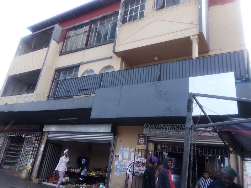 A multi-story commercial building facade featuring ground-level retail units with metal roller shutters and upper-level balconies with security railings.