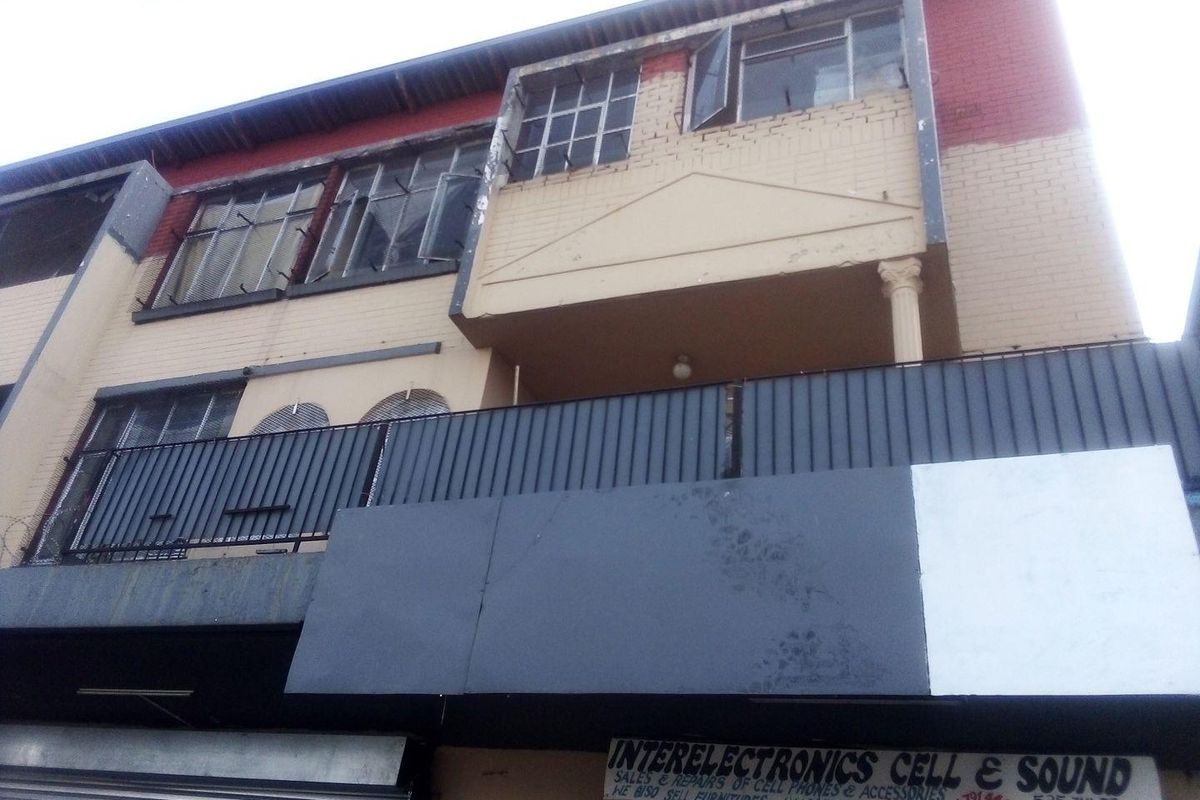 Front elevation of a commercial building featuring a ground-level storefront with security shutters and an upper-level balcony with steel railings.