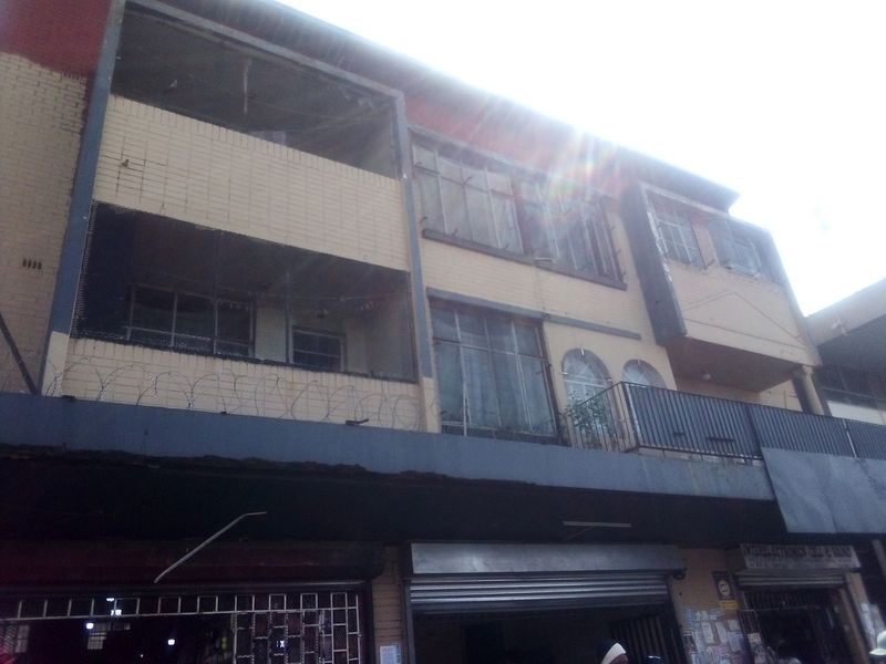 Exterior view of a multi-story commercial building featuring brick facade, balconies with metal railings, and ground-level security shutters.