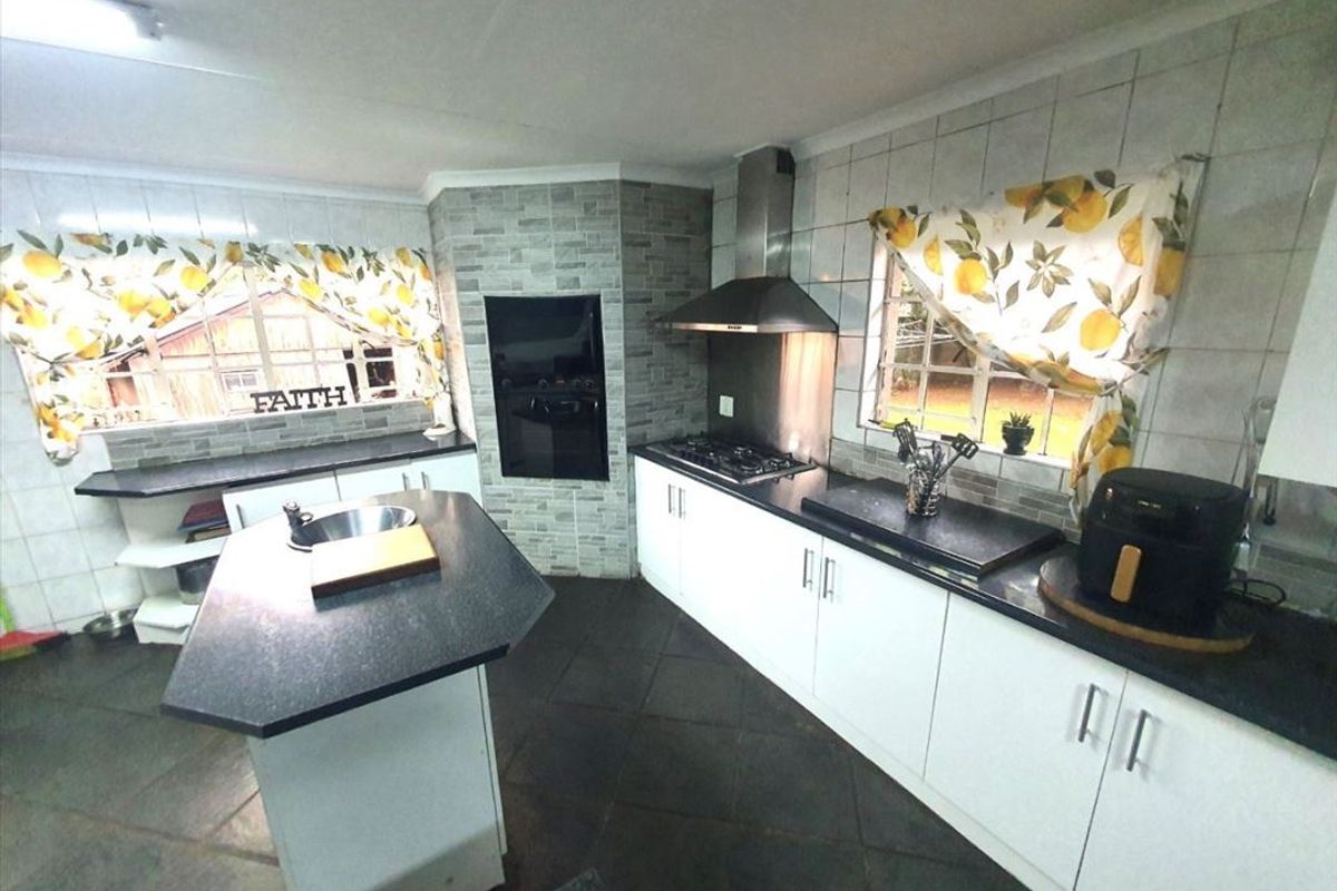A functional kitchen featuring a central island, built-in oven, gas hob with extractor fan, stone countertops, and ample cabinetry with tiled splashbacks.