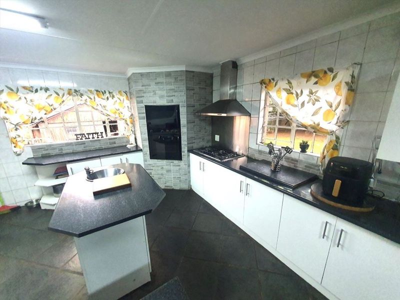 A functional kitchen featuring a central island, built-in oven, gas hob with extractor fan, stone countertops, and ample cabinetry with tiled splashbacks.