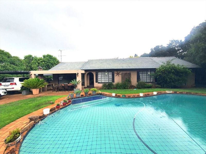 Rear view of the property featuring a swimming pool with safety net, a covered patio area, and established garden surroundings.