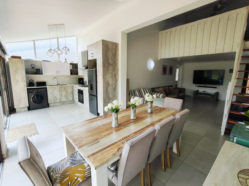 Spacious open-plan living area featuring a modern kitchen with subway tile backsplash, integrated appliances, tiled flooring, and a mezzanine level with staircase access.