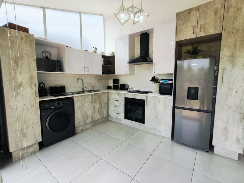 Modern kitchen featuring contemporary cabinetry, subway tile backsplash, integrated oven and hob, and sleek tiled flooring with ample natural light.