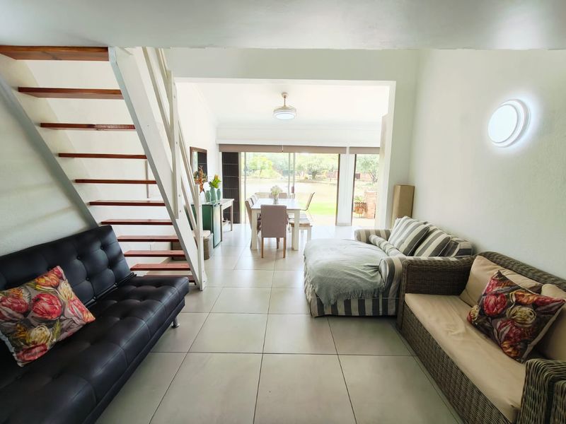 Open-plan living and dining area featuring ceramic floor tiles, an open-tread staircase, and large sliding glass doors leading to the outdoor space.