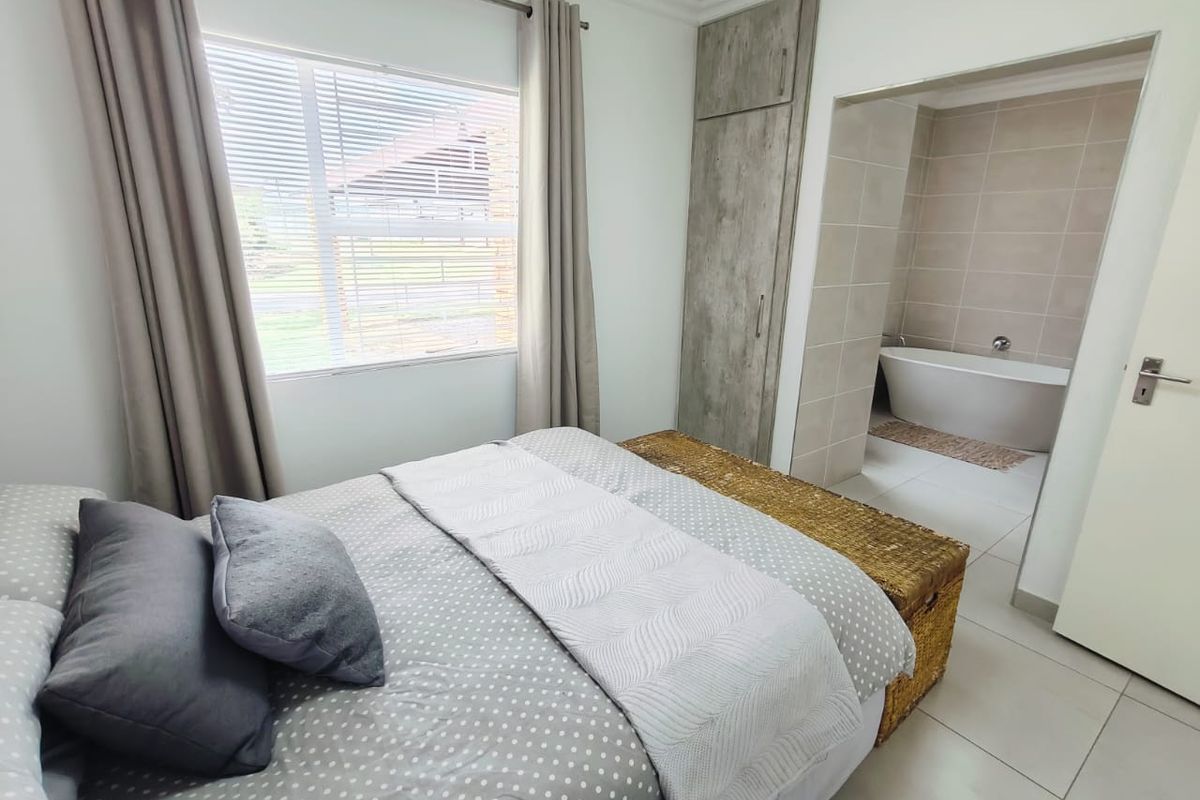 A well-maintained bedroom featuring built-in cupboards, tiled flooring, and an open-plan en-suite bathroom with a modern freestanding bathtub.
