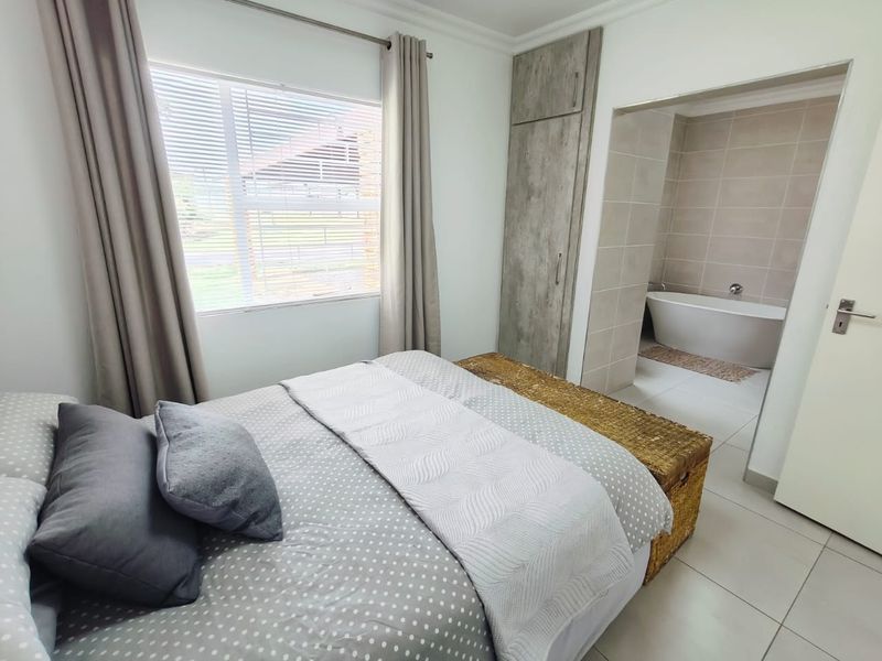 A well-maintained bedroom featuring built-in cupboards, tiled flooring, and an open-plan en-suite bathroom with a modern freestanding bathtub.