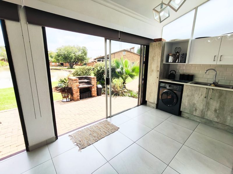 Modern kitchen featuring built-in cabinetry, subway tile backsplash, and seamless flow to an outdoor patio area with a built-in brick braai.