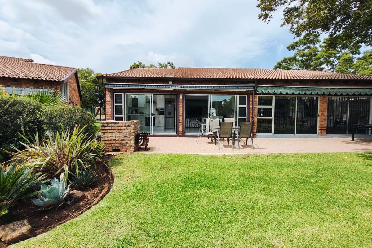 Rear view of the property featuring a paved patio, built-in brick braai, retractable awning, and direct access to the interior through sliding glass doors.