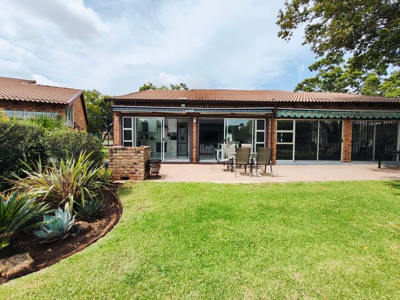 Rear view of the property featuring a paved patio, built-in brick braai, retractable awning, and direct access to the interior through sliding glass doors.