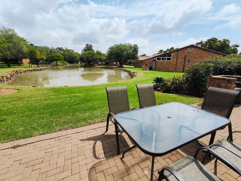 A paved outdoor patio area featuring a built-in brick braai, overlooking a scenic garden and pond.