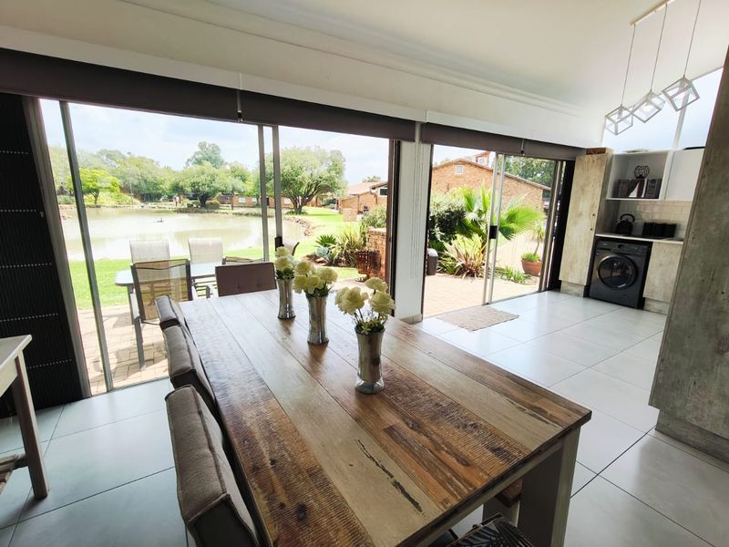 Bright open-plan living and dining area featuring large sliding doors that open to a patio with scenic lake views and modern tiled flooring.
