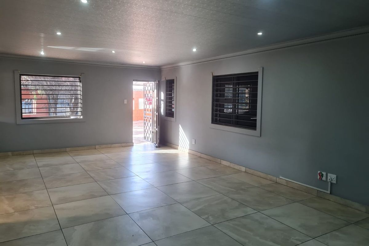 A spacious, empty living area featuring neutral tiled flooring, recessed downlighting, and secure window bars, offering a clean canvas for interior design.