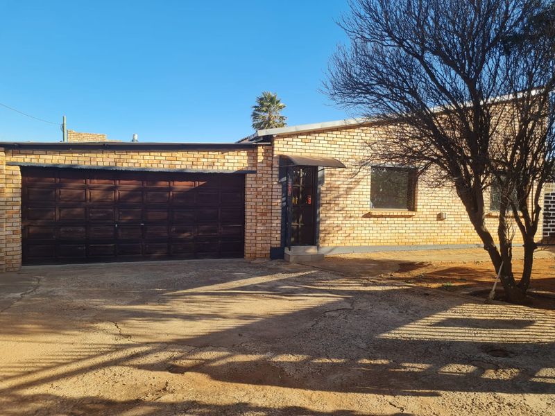 Front exterior view of a face brick house featuring a double garage, concrete driveway, and security entrance gate.