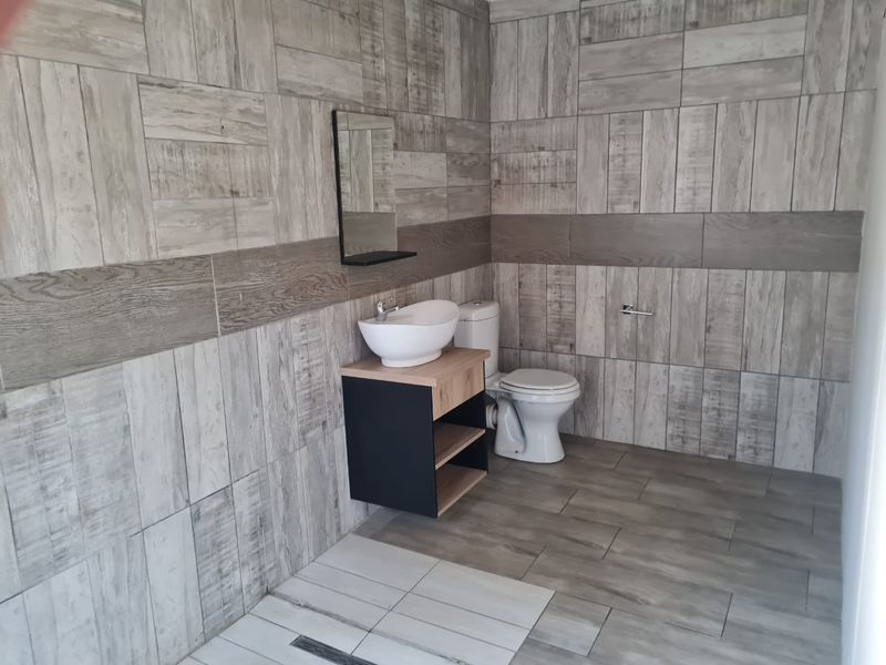 A modern, well-maintained bathroom featuring wood-look wall and floor tiles, a contemporary vessel sink vanity, and a standard toilet.