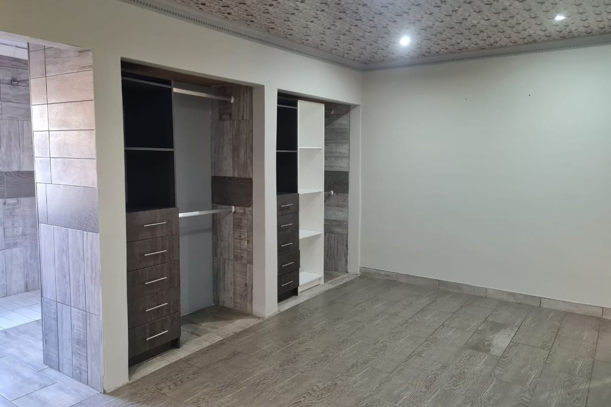 Spacious bedroom featuring modern built-in cupboards, wood-look tiled flooring, and a unique decorative ceiling finish with recessed lighting.