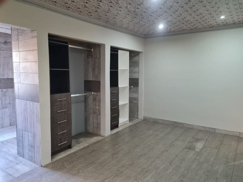 Spacious bedroom featuring modern built-in cupboards, wood-look tiled flooring, and a unique decorative ceiling finish with recessed lighting.