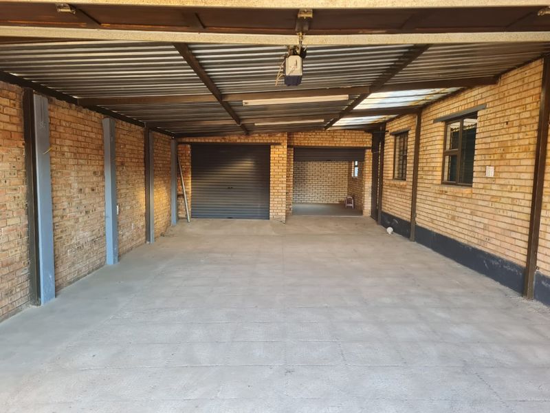 Spacious, functional garage featuring exposed brick walls, concrete flooring, and secure roller shutter doors, providing ample space for vehicle storage.