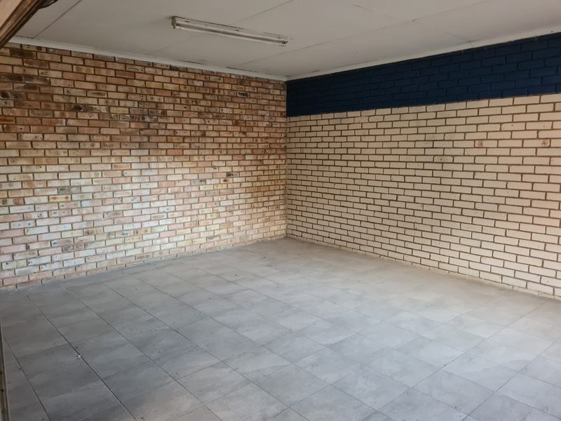 An empty garage space featuring exposed brick walls, tiled flooring, and a functional overhead fluorescent light fixture.
