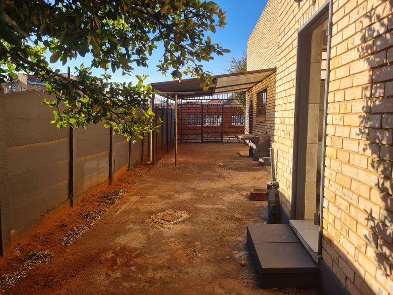 Rear exterior area featuring a concrete patio, covered walkway, and face brick walling, providing a functional outdoor space with potential for landscaping improvements.