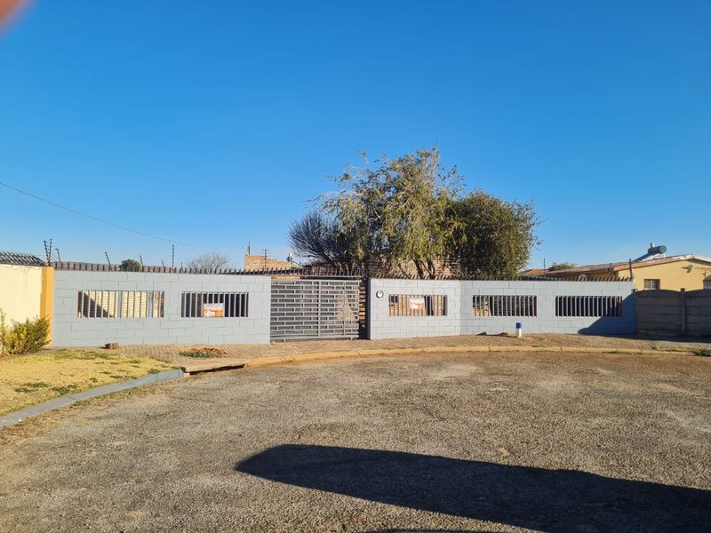 Front view of the property featuring a secure perimeter wall with integrated metal security gates and electric fencing, complemented by a paved driveway area.