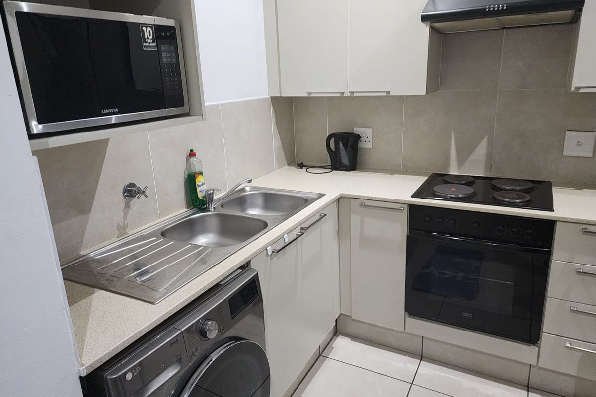 Compact kitchen featuring modern cabinetry, stone countertops, built-in oven, electric hob, extractor fan, and integrated space for a washing machine.