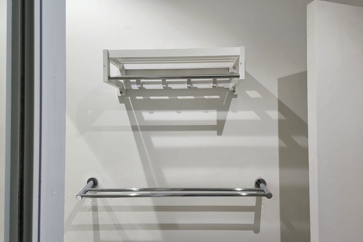 A clean bathroom wall featuring a white wall-mounted storage rack and a modern chrome double towel rail.