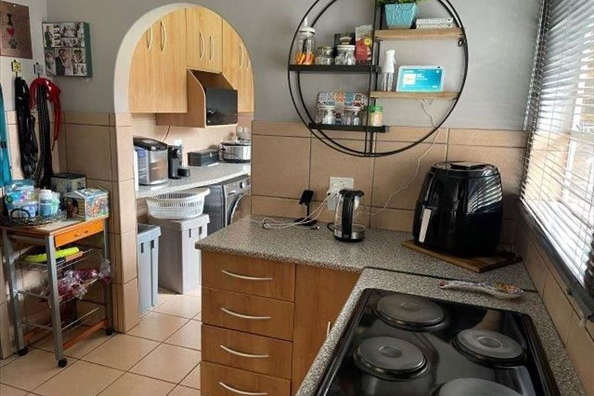 A functional kitchen featuring wood-finish cabinetry, tiled backsplash, and an electric hob, with an arched opening leading to a secondary utility or laundry area.