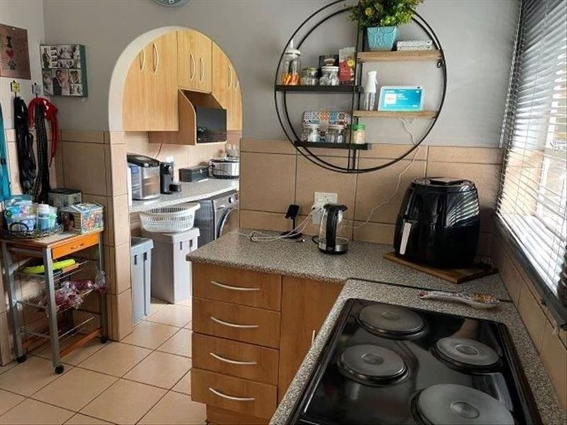 A functional kitchen featuring wood-finish cabinetry, tiled backsplash, and an electric hob, with an arched opening leading to a secondary utility or laundry area.