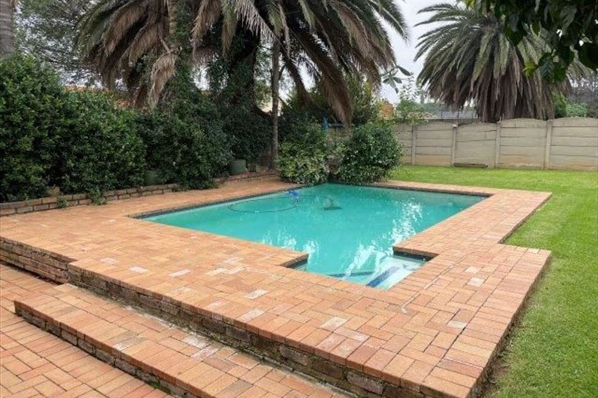A backyard swimming pool area featuring a brick-paved surround, lawn, and precast concrete boundary wall.