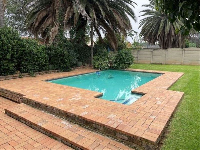 A backyard swimming pool area featuring a brick-paved surround, lawn, and precast concrete boundary wall.