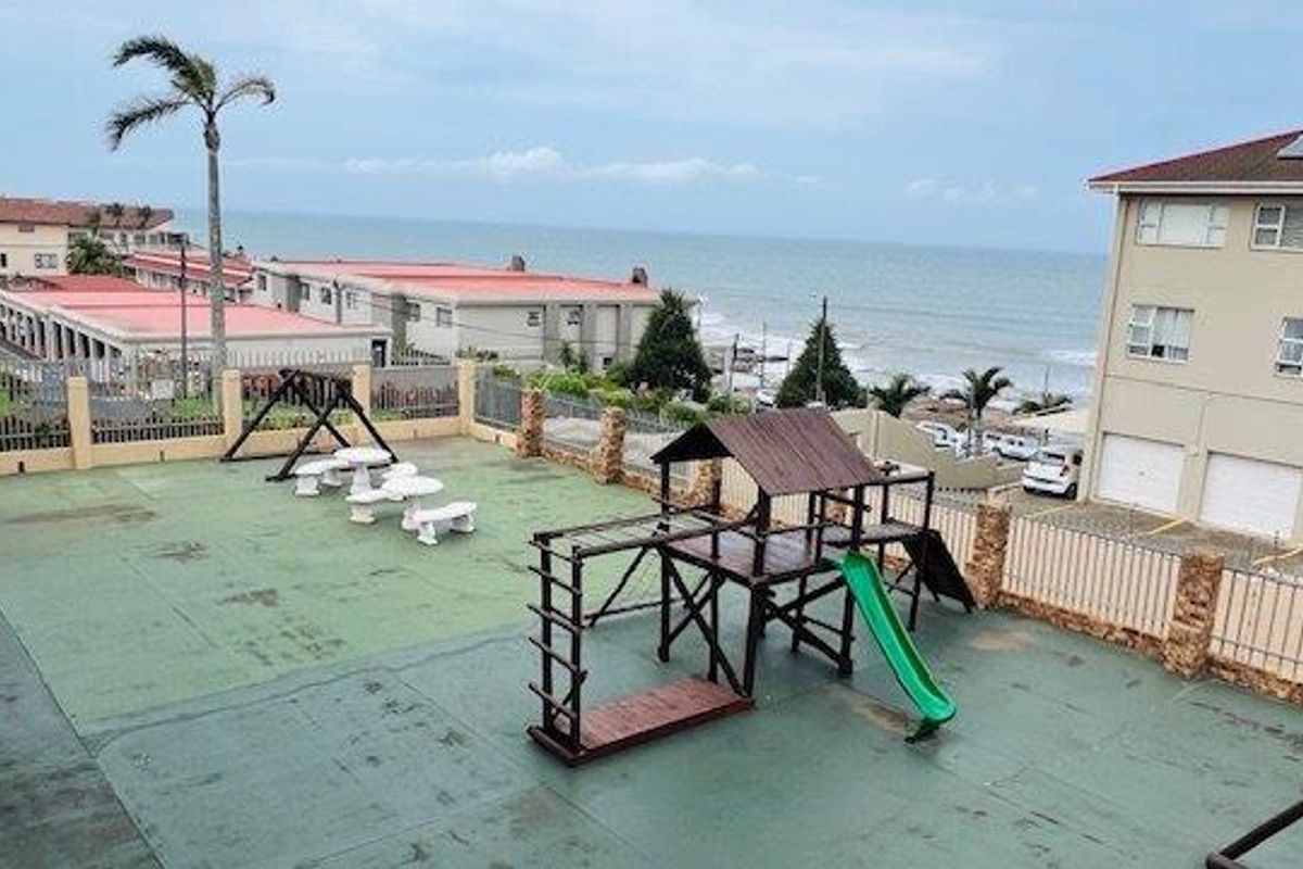 Communal outdoor play area featuring a jungle gym and seating, set within a residential complex with ocean views.