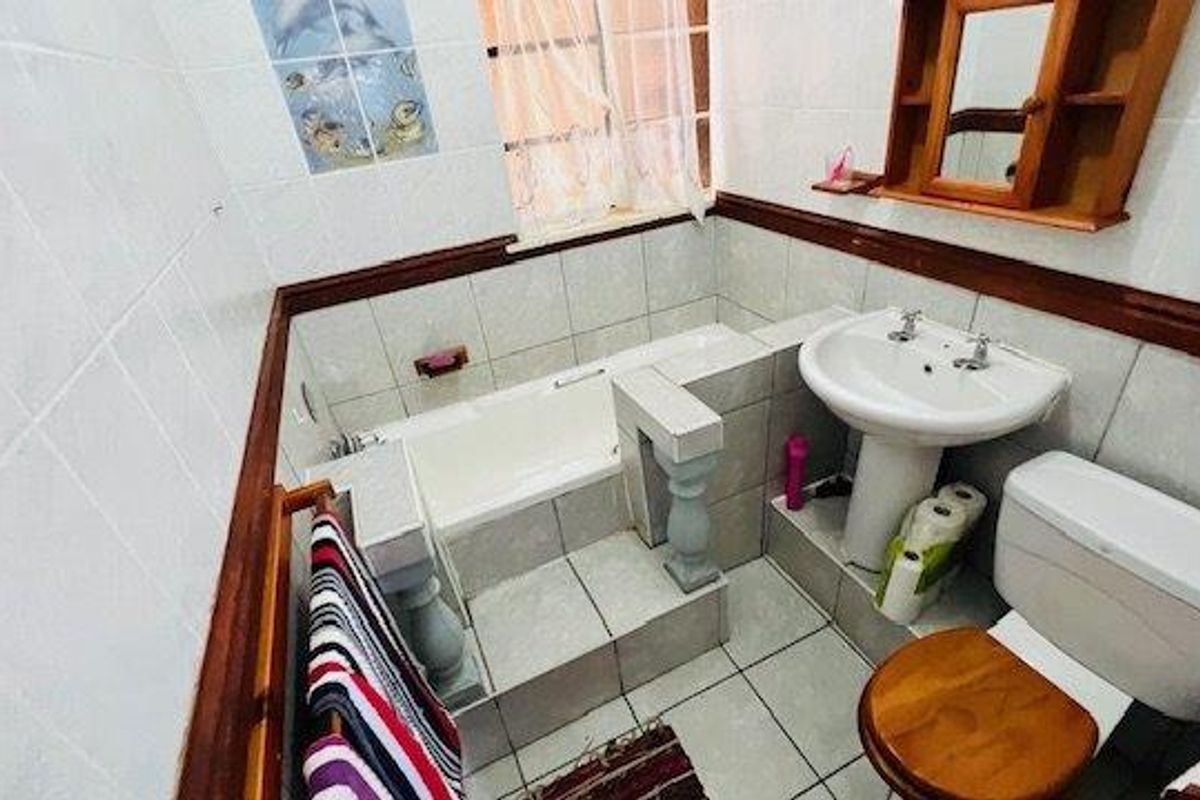 A compact bathroom featuring a tiled bathtub, pedestal basin, and toilet with classic finishes and wooden accents.