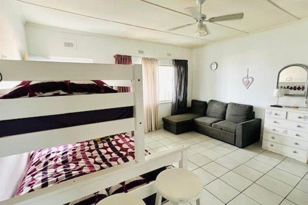 A spacious bedroom featuring tiled flooring, a ceiling fan, and large windows allowing for natural light.