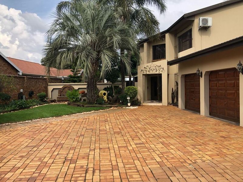 Front view of the property featuring a spacious brick-paved driveway, double garage, and a landscaped garden with a water feature.