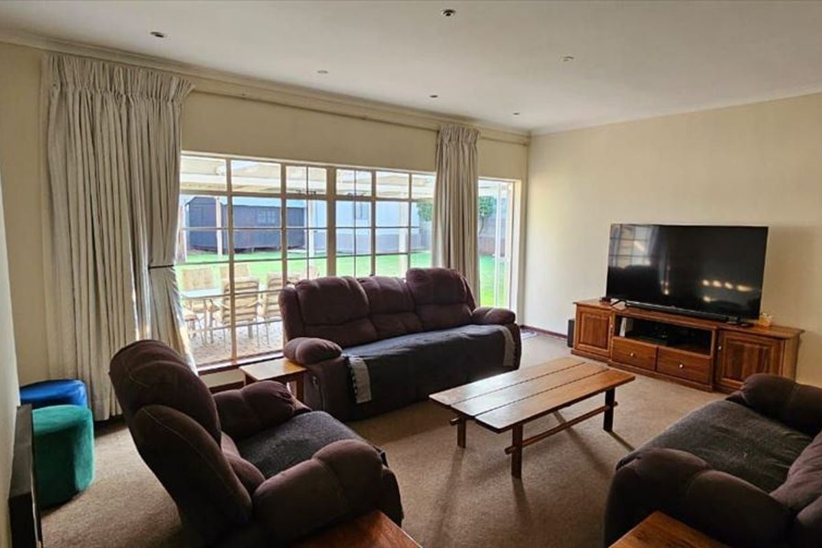 Spacious living room featuring carpeted flooring, recessed downlights, and a large sliding glass door providing direct access to the rear garden area.