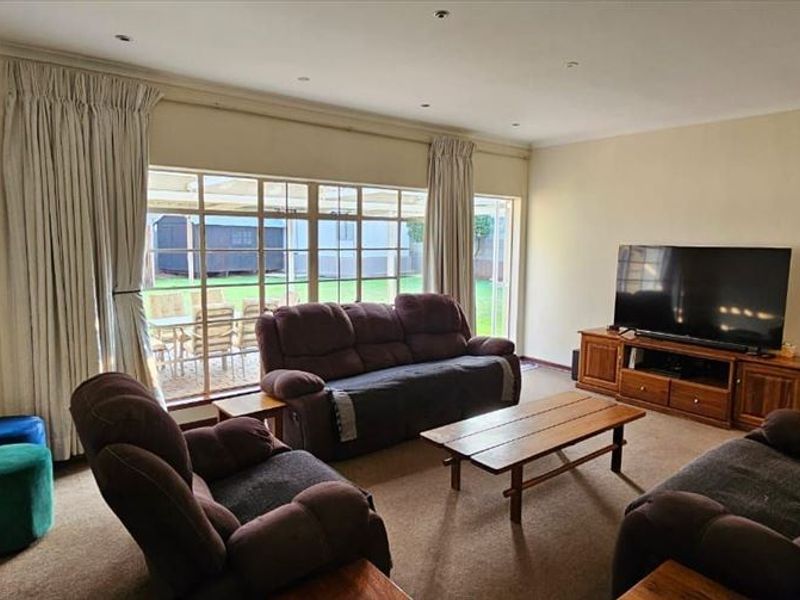 Spacious living room featuring carpeted flooring, recessed downlights, and a large sliding glass door providing direct access to the rear garden area.