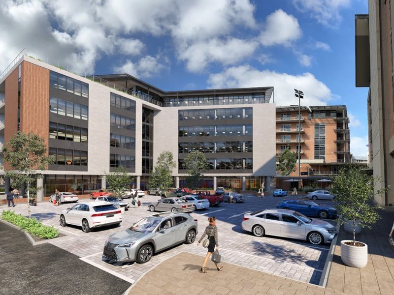 A modern multi-story commercial office building featuring a glass and brick facade with an integrated paved parking area.