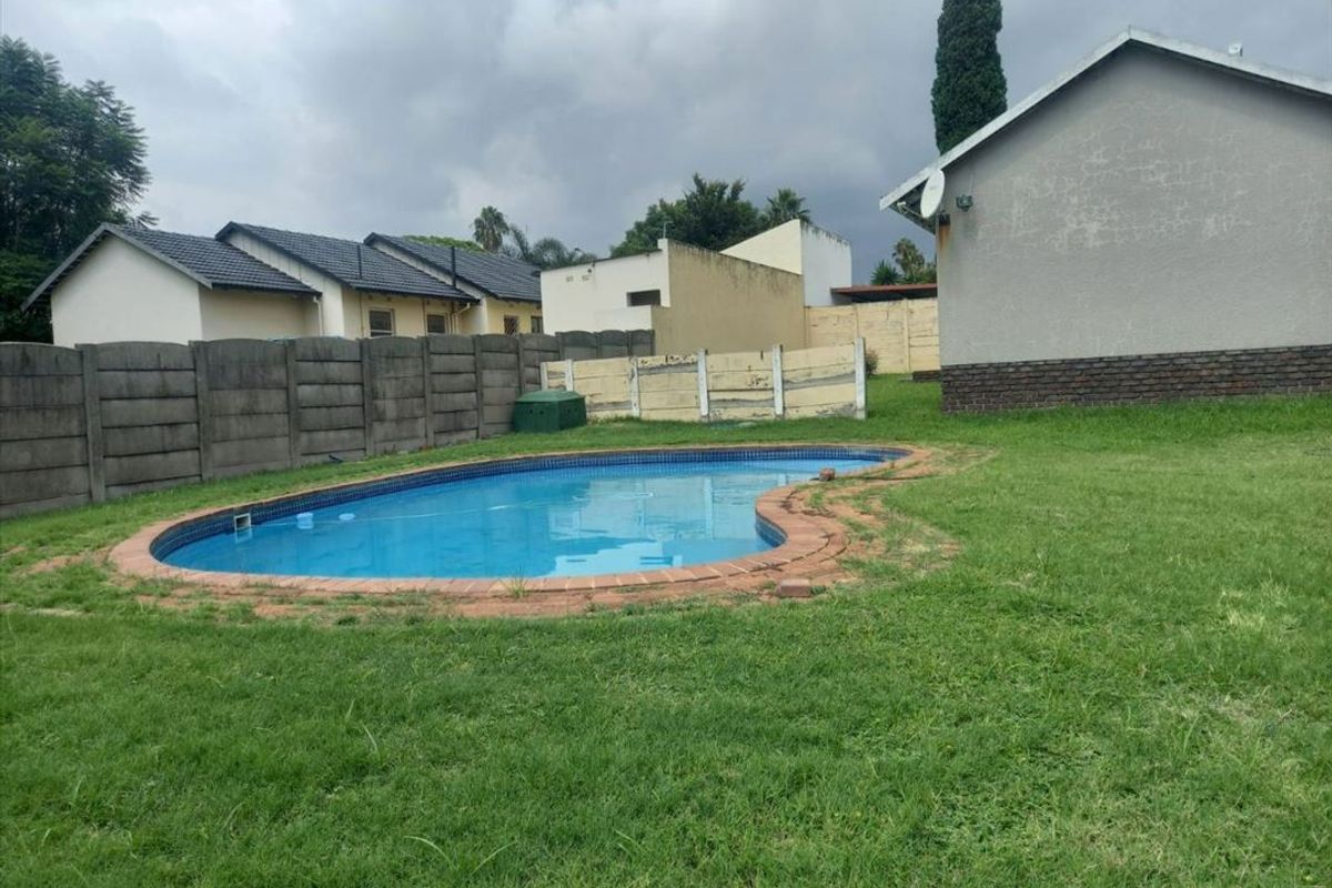 Rear garden area featuring a swimming pool with brick coping, enclosed by precast concrete boundary walls and a lawned yard.