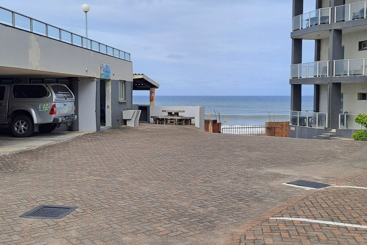 Exterior view of an apartment complex parking area featuring paved surfaces, covered parking bays, and direct access to the coastal beachfront.