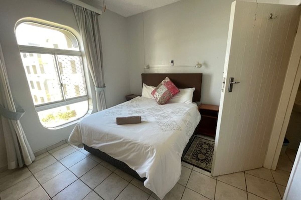 A bedroom featuring tiled flooring and a distinctive arched window, providing natural light and a functional layout.