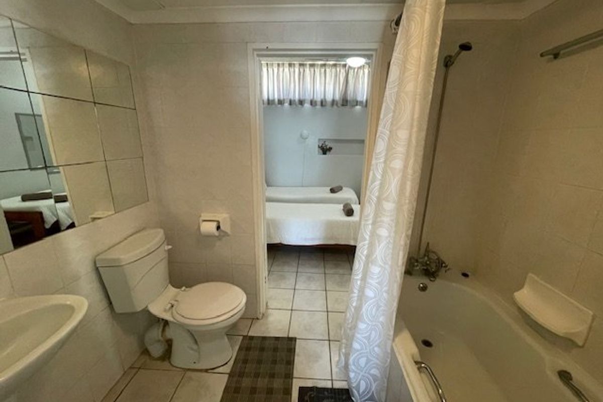A dated bathroom featuring a bathtub with shower attachment, pedestal basin, and toilet, with tiled finishes throughout and direct access to an adjacent bedroom.
