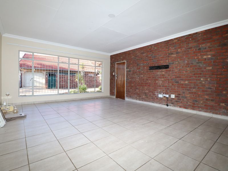 Spacious living room featuring a prominent exposed brick feature wall, large windows with security bars, and neutral ceramic floor tiling.