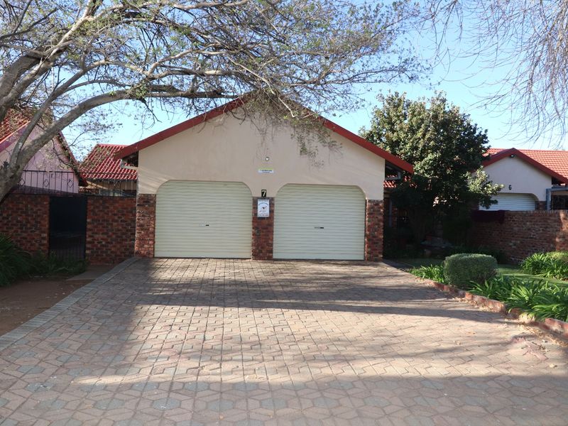 A double garage with roller doors and a paved driveway, situated in a residential townhouse complex.