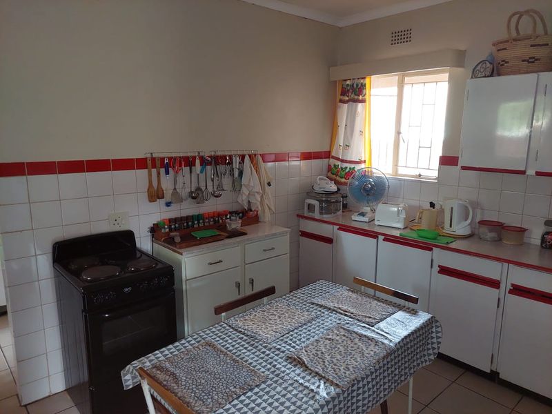 A functional kitchen featuring white cabinetry with red trim, tiled splashbacks, and a freestanding electric stove.