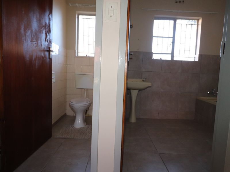 A functional bathroom featuring a pedestal basin, toilet, and tiled flooring, with a separate partitioned area for privacy.