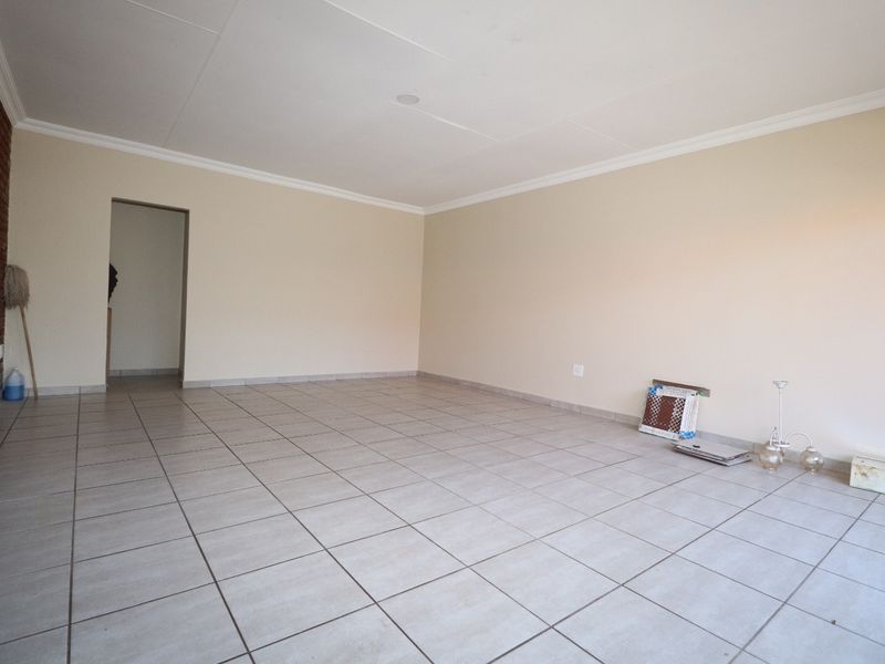 A spacious, empty living area featuring neutral tiled flooring and a decorative exposed brick feature wall, offering a versatile blank canvas.