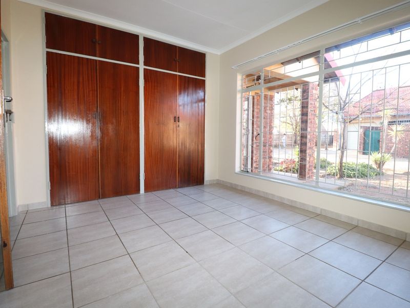A bright bedroom featuring large windows with security bars, tiled flooring, and built-in wooden cupboards.