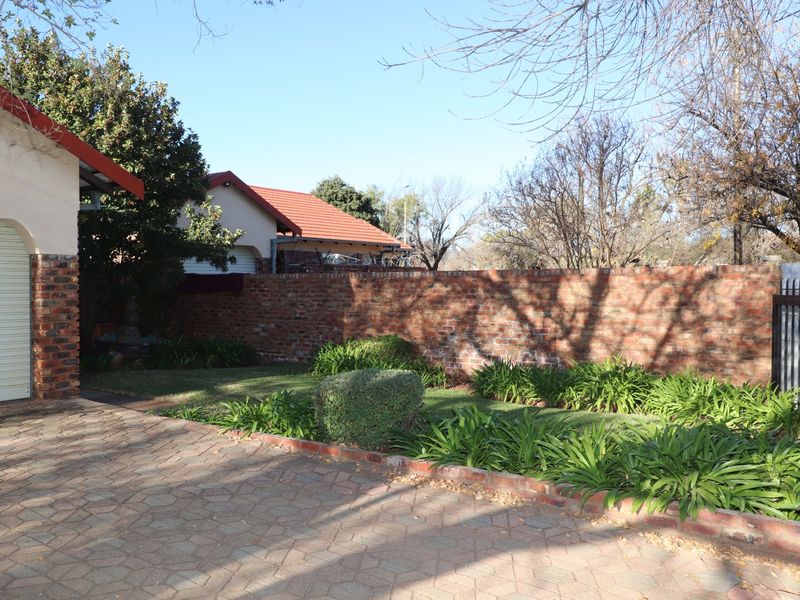 A view of the property's exterior featuring a paved driveway, a garage with a roller door, a brick boundary wall, and a landscaped garden area.