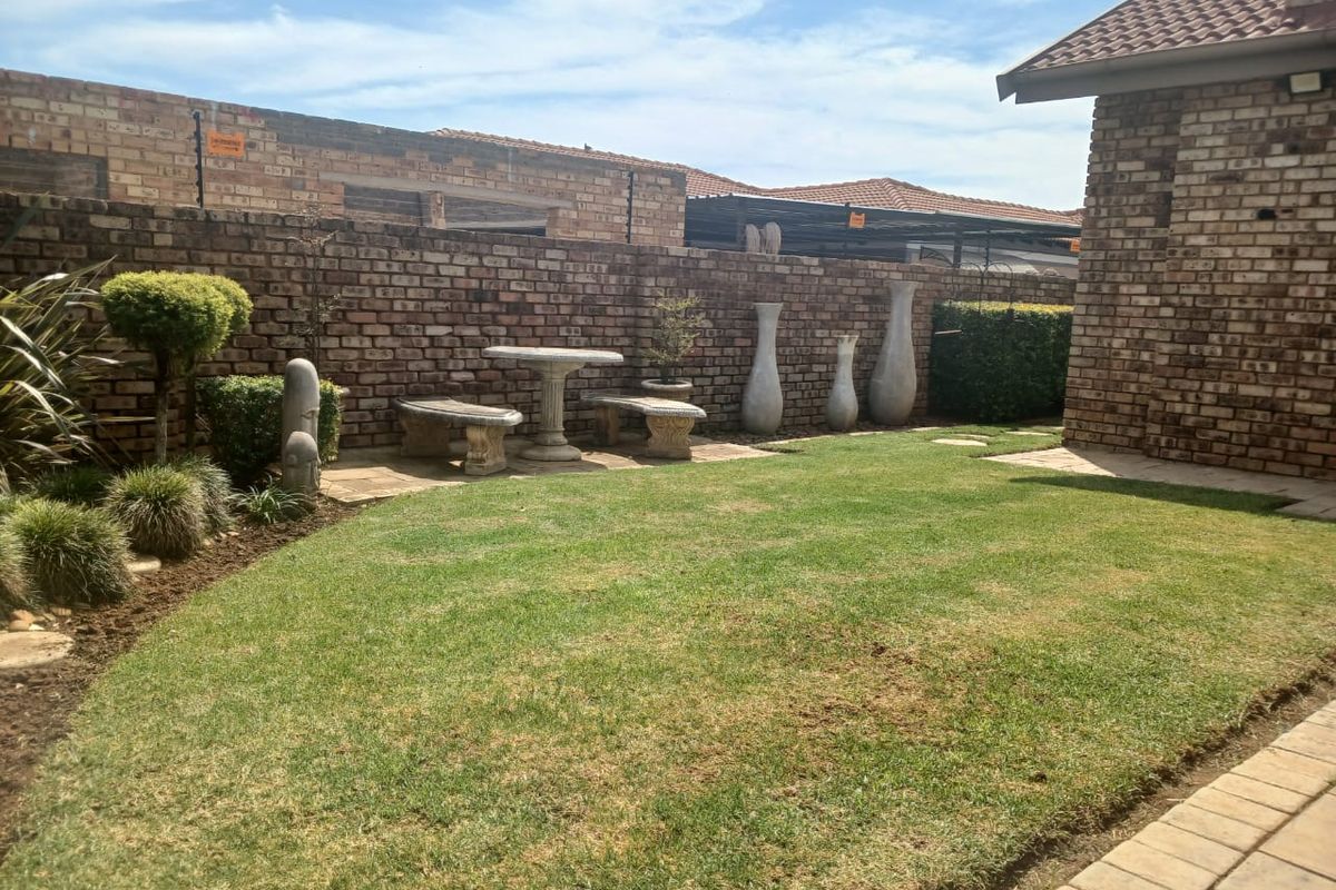 A well-maintained rear garden featuring a manicured lawn, face brick boundary walls with electric fencing, and a paved walkway.